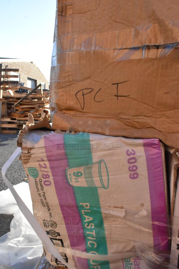 Cardboard boxes labeled "Plastic Cups" and "Quality Paper Goods, Inc." showing signs of wear and denting. Contains cups, containers, and napkins.