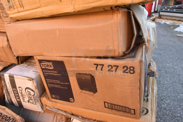 Stacked boxes containing scratch and dent items, including a Tork mechanical hand towel roll dispenser in original packaging.