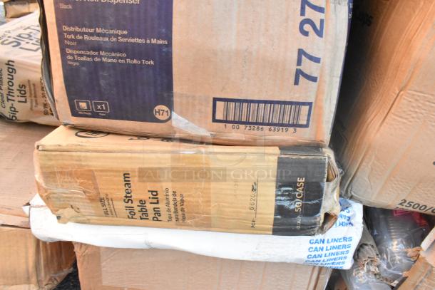 Stack of boxes containing assorted new scratch and dent items, including a mechanical towel dispenser marked "Tork," and foil steam pan lids.
