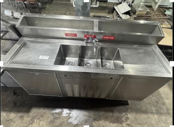 Three-compartment stainless steel commercial sink with attached two-door cooler, featuring rinse and sanitize labels, in good condition.