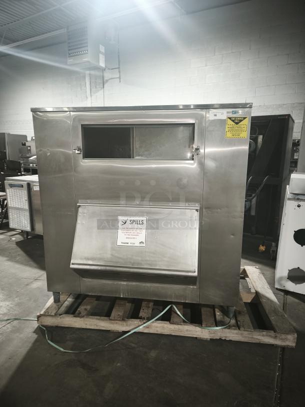 MGR Equipment SP-1650-SS ice storage bin, stainless steel, label indicating safety advice, placed on a wooden pallet.