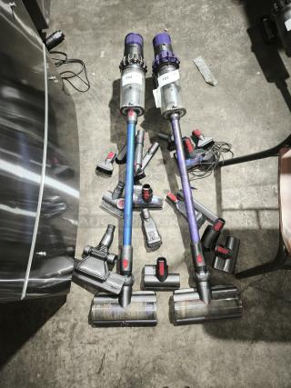 Dyson V11 Torque Drive PLUS cordless vacuum cleaners with multiple attachments, labeled 103 and 104, displayed on the floor.