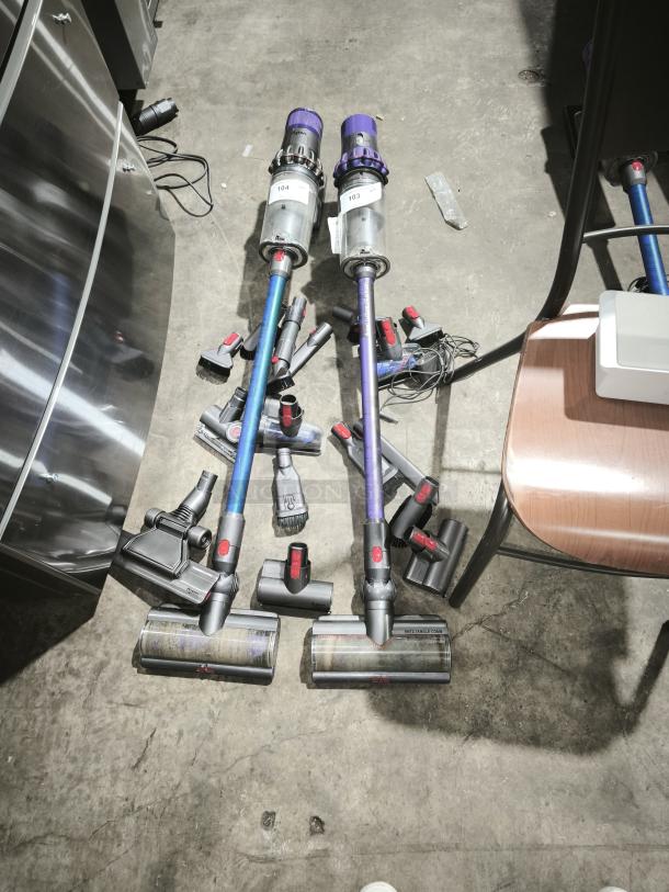 Two Dyson V11 Torque Drive PLUS cordless vacuums with attachments, numbered labels, in good condition on concrete floor.