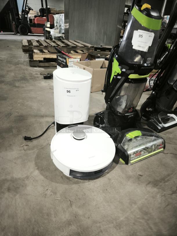 White DEEBOT robotic vacuum with charging station on concrete floor. Features minimal labels; appears in good condition.