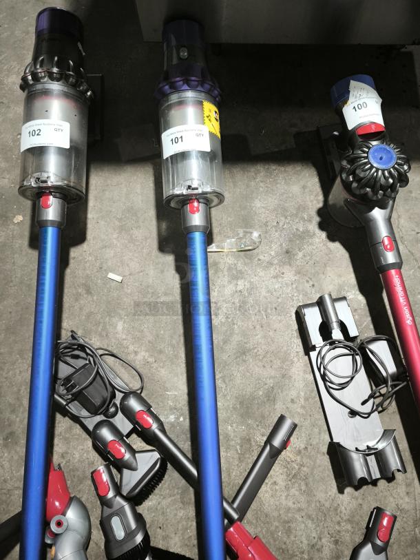 Dyson V11 Torque Drive PLUS cordless vacuum, blue and red, with attachments. Visible tags show auction labels 100, 101, 102.