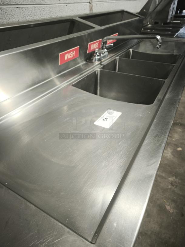 Three compartment stainless steel sink with labeled wash, rinse, sanitize sections and attached faucet. Includes 2-door cooler.