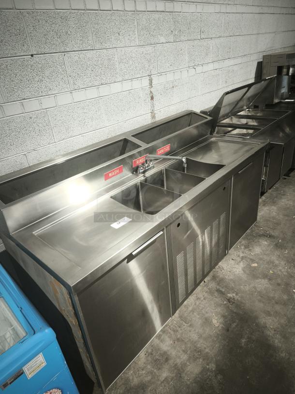 Stainless steel three-compartment sink with red wash, rinse, sanitize labels, and two-door cooler, ideal for commercial use.