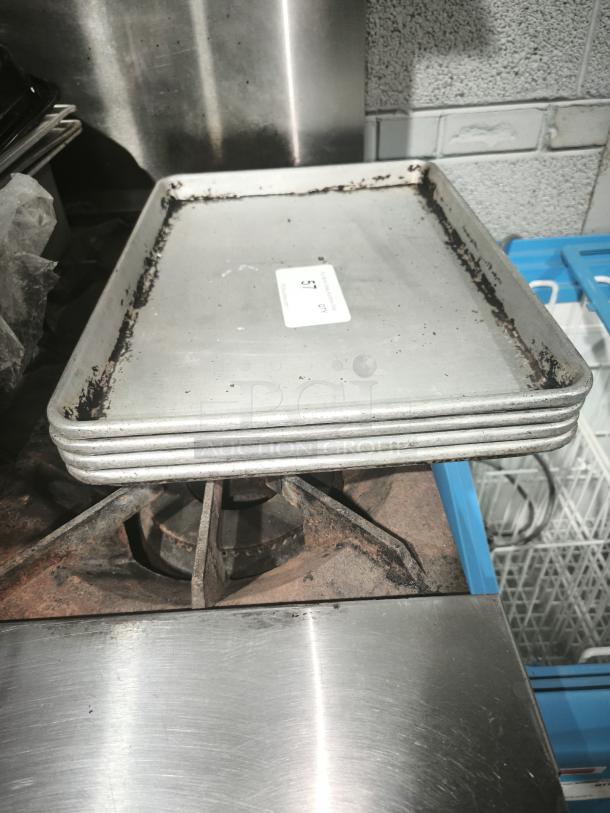 Stack of commercial heavy-duty aluminum half-sheet pans showing signs of use; label marked "51" visible.