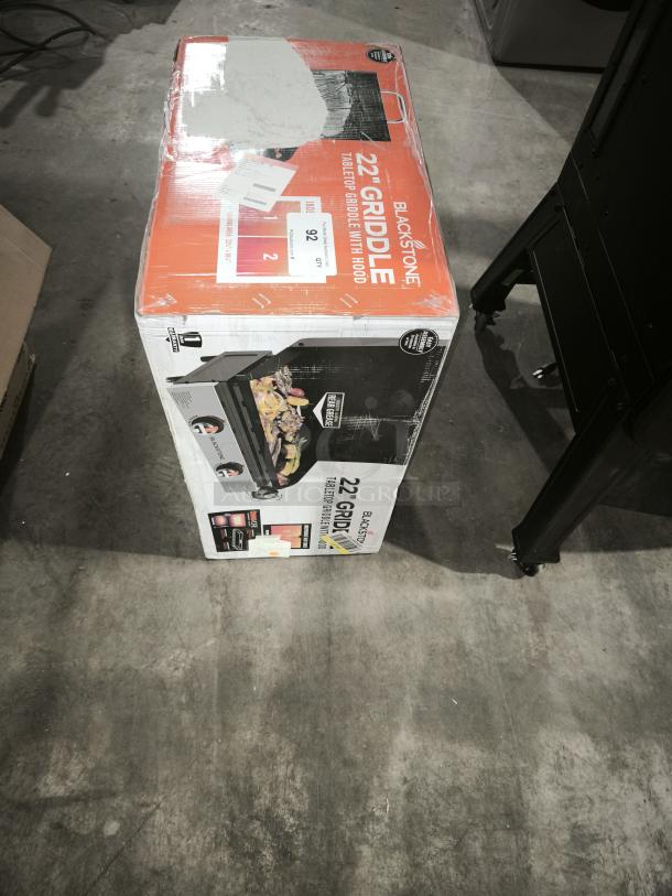 Brand new Blackstone 22" Tabletop Griddle with Hood, Model 2205, in sealed packaging, features cooking area and portability.