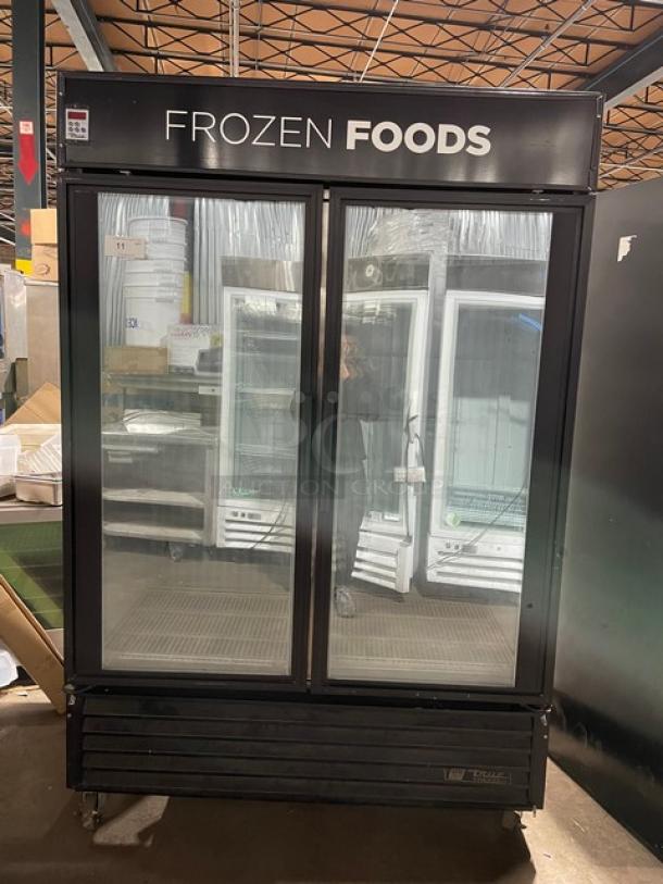 True GDM-49F commercial black double glass door freezer; features poly-coated wire rack, casters, and "Frozen Foods" label.