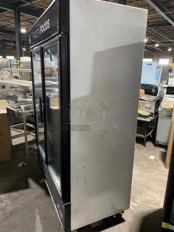 True GDM-49F commercial freezer with double glass doors, poly coated racks, and casters. Black exterior, model SN: 1-4780407.