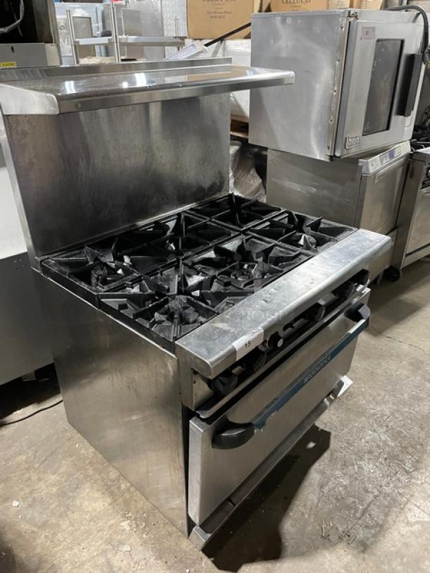 Radiance by Turbo Air commercial 6-burner stainless steel range/oven combo with back splash, overhead salamander shelf, and wired oven rack, on legs. Natural gas powered.