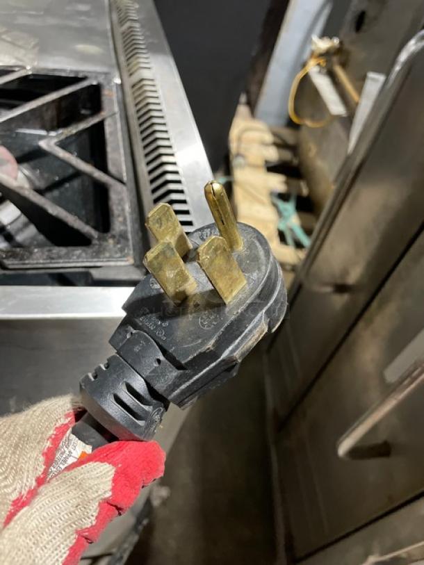 Monogram commercial stainless steel 4-burner gas range/oven combo, features wired oven rack and legs. Plug connectors visible.