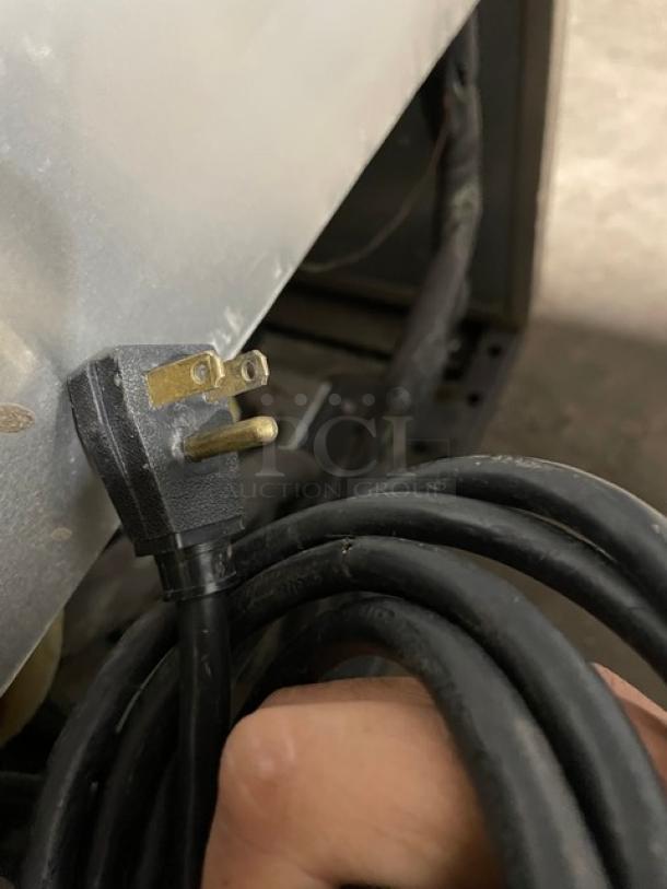 Black power plug attached to a cable, held near a stainless steel surface, part of a commercial freezer.