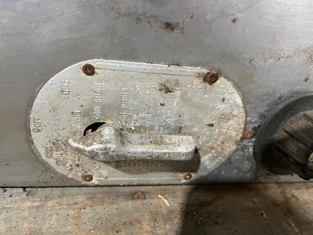 Bakers Pride pizza oven control panel showing metal lever and worn label with technical specs. Steel surface, used condition.