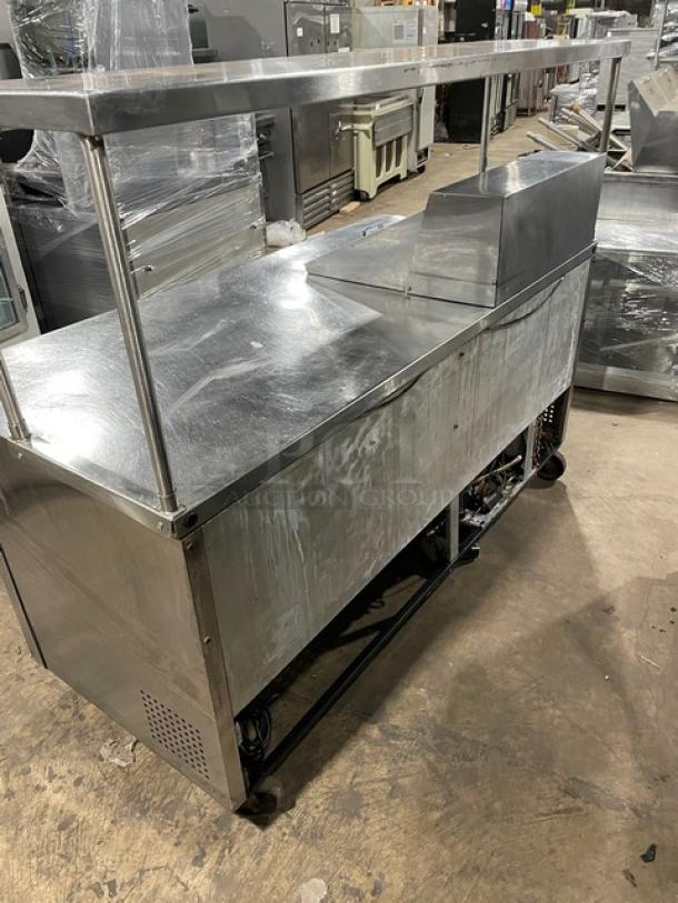 True TSSU-72-12M-B stainless steel 3-door refrigerated prep table with overhead shelf and wire rack, on casters.