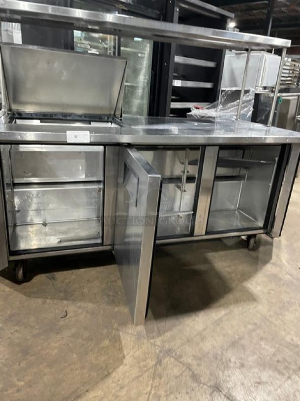 True TSSU-72-12M-B 3-door refrigerated prep table, stainless steel, overhead shelf, wired rack, on casters, good condition.