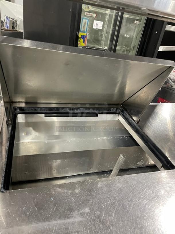 True TSSU-72-12M-B stainless steel refrigerated prep table, open lid view, with overhead shelf and wired rack, on casters.