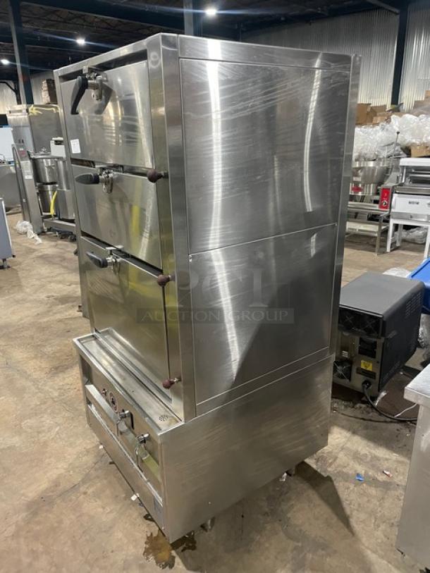 Commercial stainless steel 3-compartment seafood steamer, natural gas powered, with individual controls and wired oven rack. Mounted on legs.