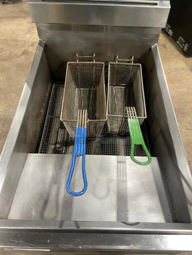 Commercial stainless steel natural gas deep fryer with backsplash, basket hanger, two fry baskets, on sturdy legs.