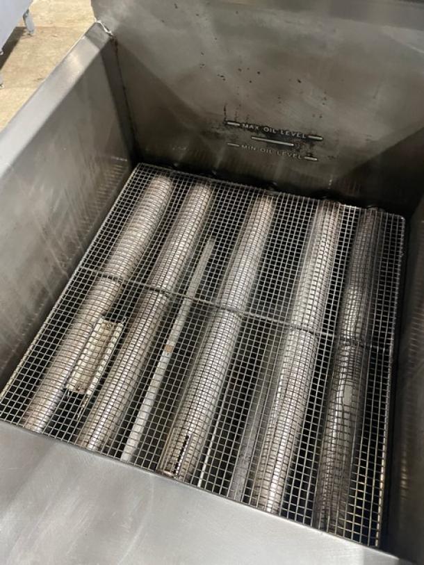 Commercial stainless steel natural gas deep fat fryer with backsplash, basket hanger, and fry basket. Appears in used condition.