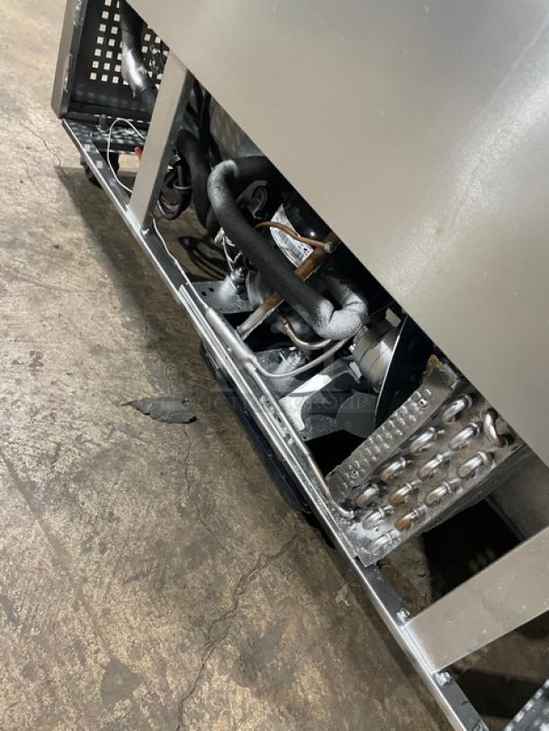 True TUC-48 commercial refrigerator underside, showing wiring and components. Stainless steel construction, on casters.