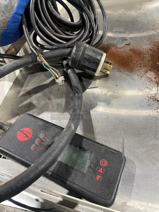 Synesso S200 Series espresso machine power cable with plug and control unit on stainless steel surface. Dust visible.