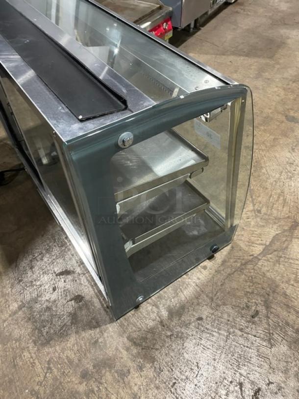 Commercial stainless steel electric heated food merchandiser with multi-level shelving and rear double glass sliding doors.
