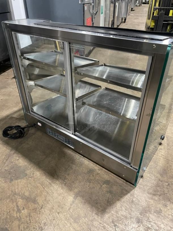 Commercial stainless steel electric heated food merchandiser display case with three shelves, rear glass sliding doors.