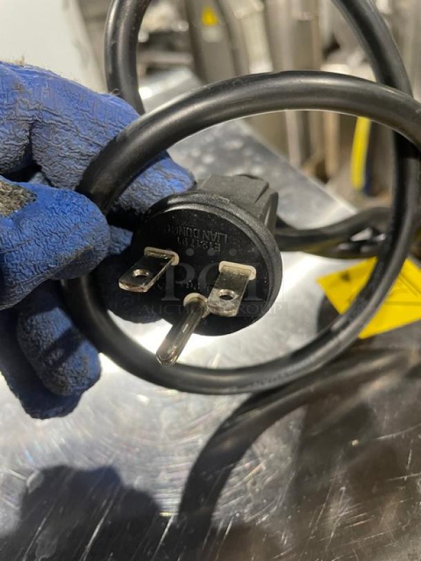 Close-up of a power plug for Cadco XAF023 convection oven, showing a three-prong design, held by a gloved hand.