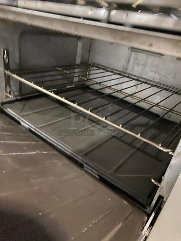 SunFire stainless steel 6-burner range/oven with backsplash, overhead salamander shelf, and wired oven rack, on casters.