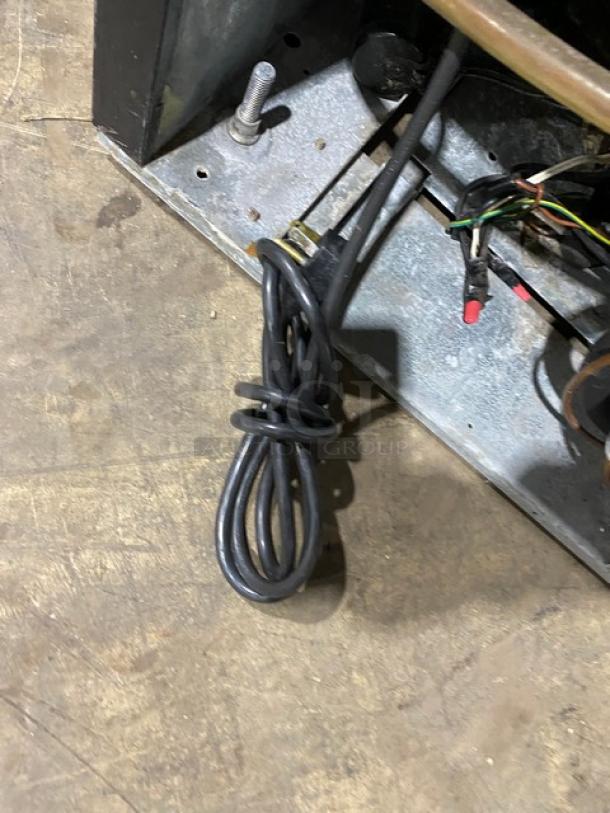 Close-up of the Beverage-Air MT27 merchandiser refrigerator's plug and wiring on a metal base. Plug neatly coiled.