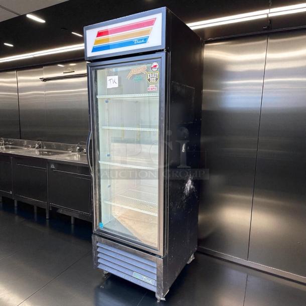A glass-front display refrigerator with stickers on the door and "True" branding above. Stainless steel interior with shelves visible.