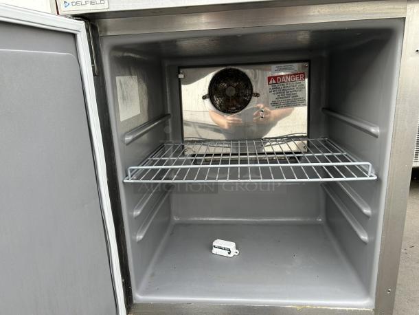 Delfield 4427NP 27"W undercounter refrigerator with one section and door, stainless steel, internal shelf, and visible safety label.