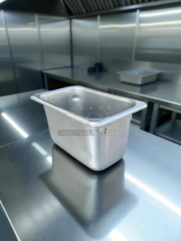 Stainless steel hotel pan, 1/9 size, 4" deep, in great condition, reflective surface in a stainless kitchen setting.