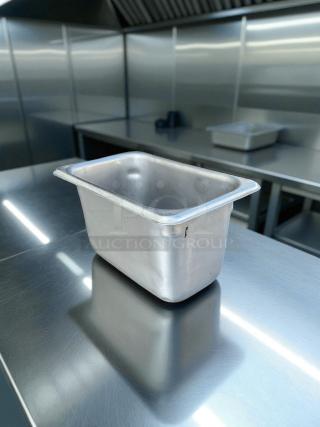 Stainless steel hotel pan, 1/9 size, 4" deep, in great condition, reflective surface in a stainless kitchen setting.