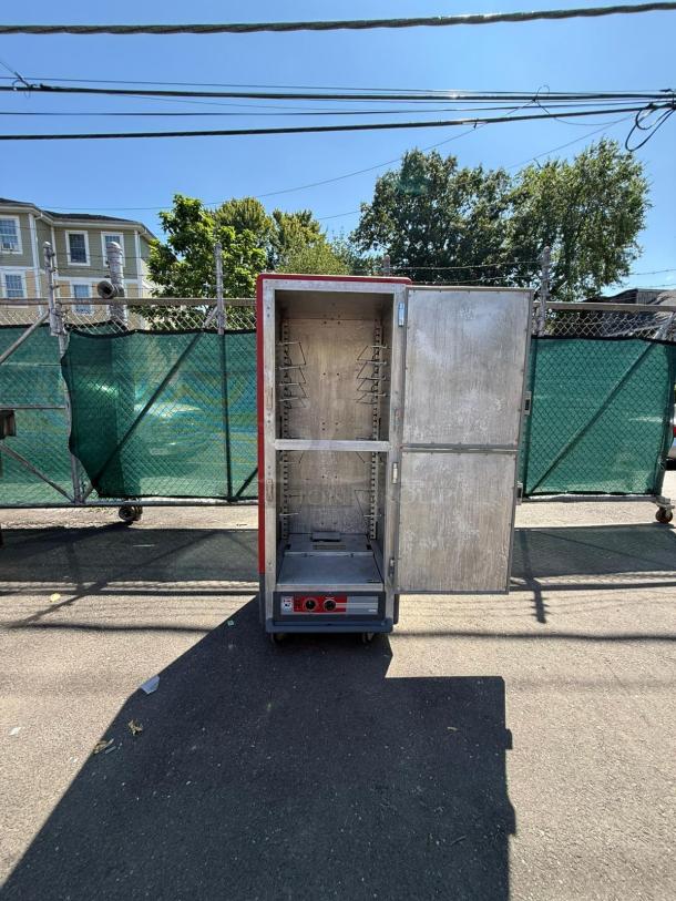 METRO C539-HDS-U red heated holding cabinet with solid Dutch doors, open view, showing interior racks, on an asphalt surface.
