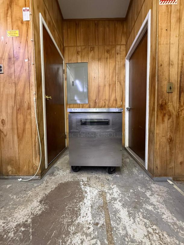 Arctic Air MCF-27U 27" undercounter freezer, stainless steel, on casters, located in a wood-paneled room.