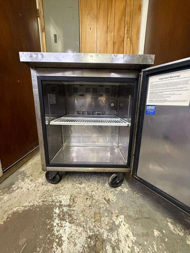 Arctic Air MCF-27U 27" Undercounter Freezer, stainless steel, open door, interior shelf, visible operational tags, on casters.