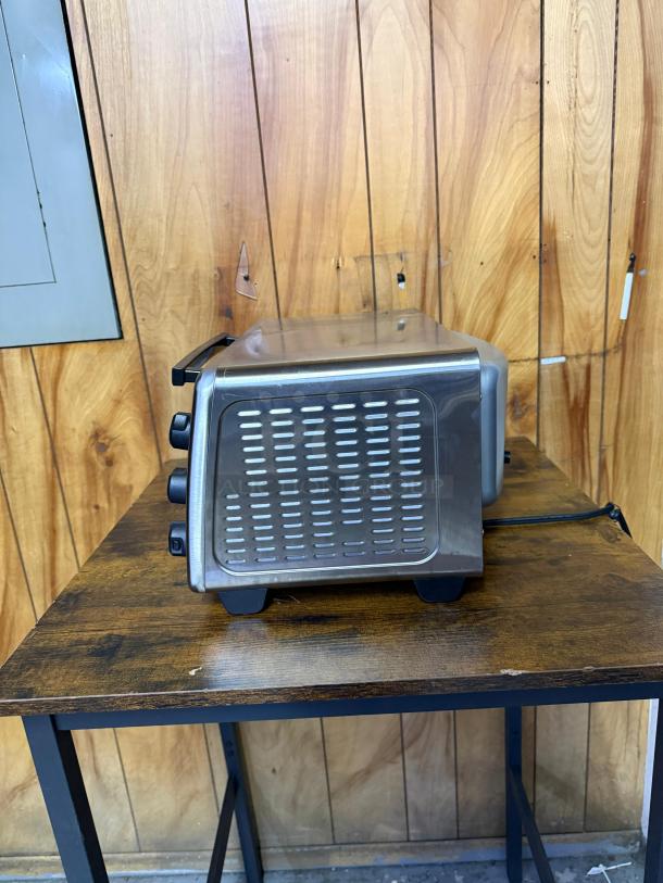 Hamilton Beach 4-slice toaster oven, stainless steel, 5 cooking modes, 1100 watts, 2 rack positions, side view on table.