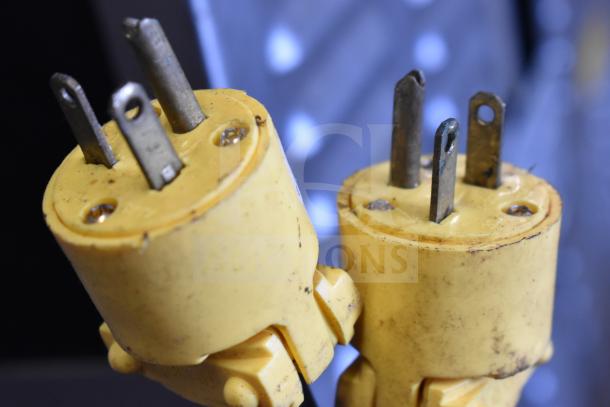 Two yellow electrical plugs with metal prongs, showing signs of wear and slight rusting.