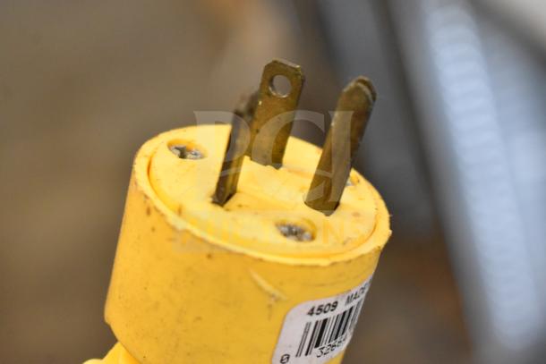 Close-up of a yellow electrical plug with metal prongs and visible screws, attached label with numbers "4509" and a barcode.