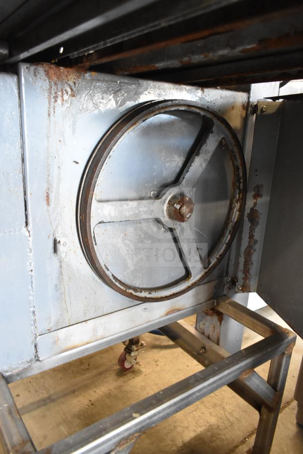 Commercial floor meat saw with metal frame and visible caster wheels, showing signs of rust and wear.