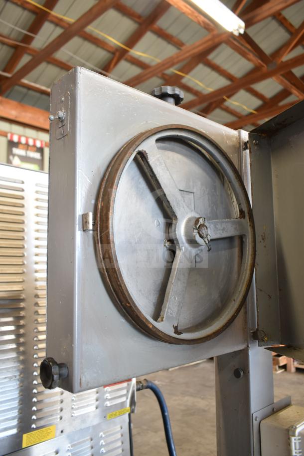 Commercial floor-style meat saw on casters, metal construction, visible wear, with large wheel mechanism, industrial setting.