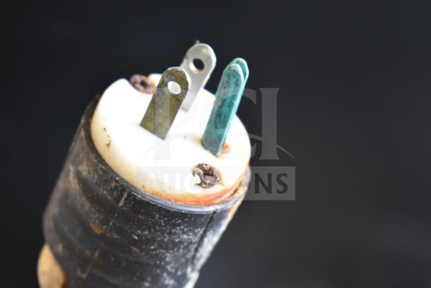 A close-up of an electrical plug with three prongs, showing signs of wear and rust, against a black background.