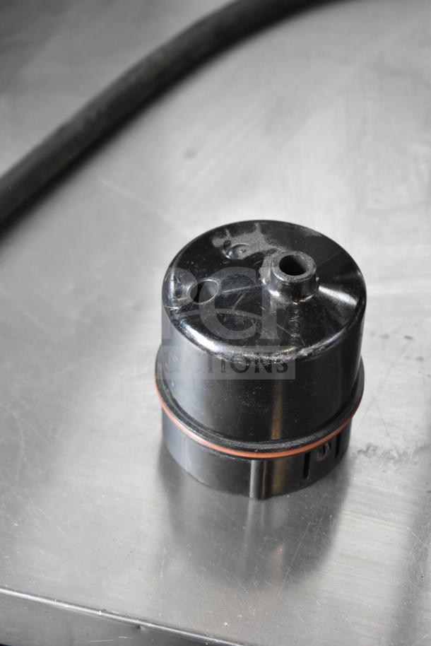 Black component part of a Clover 1S coffee brewer, showing wear, on a stainless steel surface.