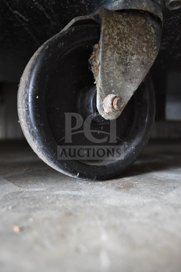Close-up of a commercial caster wheel on a 2020 Delfield D4460NP-24M-A5 prep table. Rust and wear visible on metal parts.