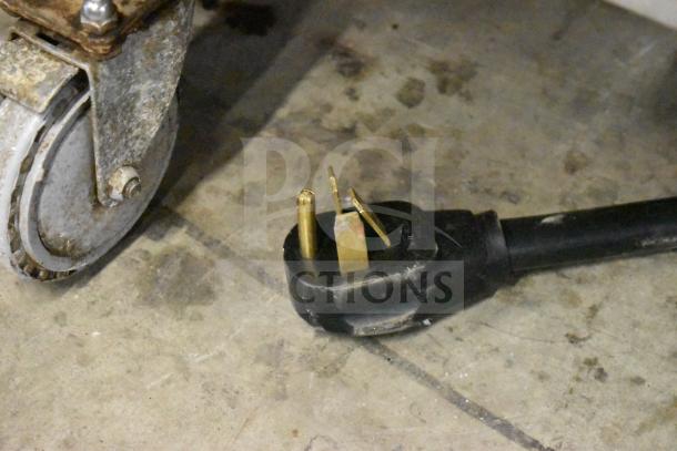 Close-up of a commercial oven caster wheel next to a 208/240V, 3-phase plug, from a Turbochef HhC2020 conveyor oven.