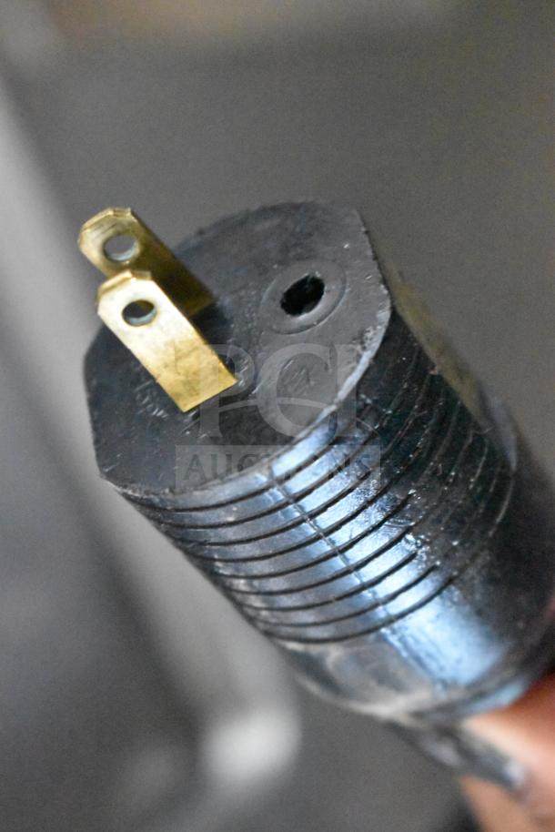 Close-up of a black electrical plug with brass prongs for the JBT 2ND-GEN-MFJ-HE Citrus Juicer, indicating a 115-volt connection.