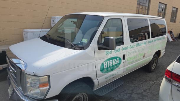 White Ford E350 van with business advertising on the side for "BISRA Glatt Kosher Meats," parked near a brick building.